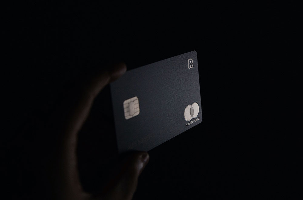 A person holding up a credit card against a black background. 