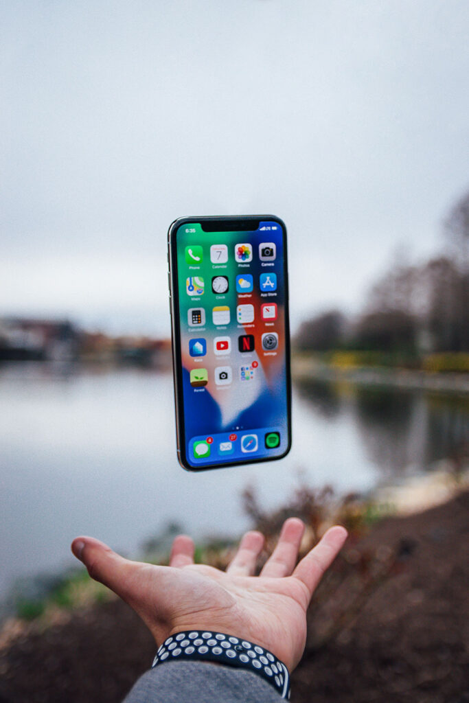 A person's hand is held out, under a floating smartphone.